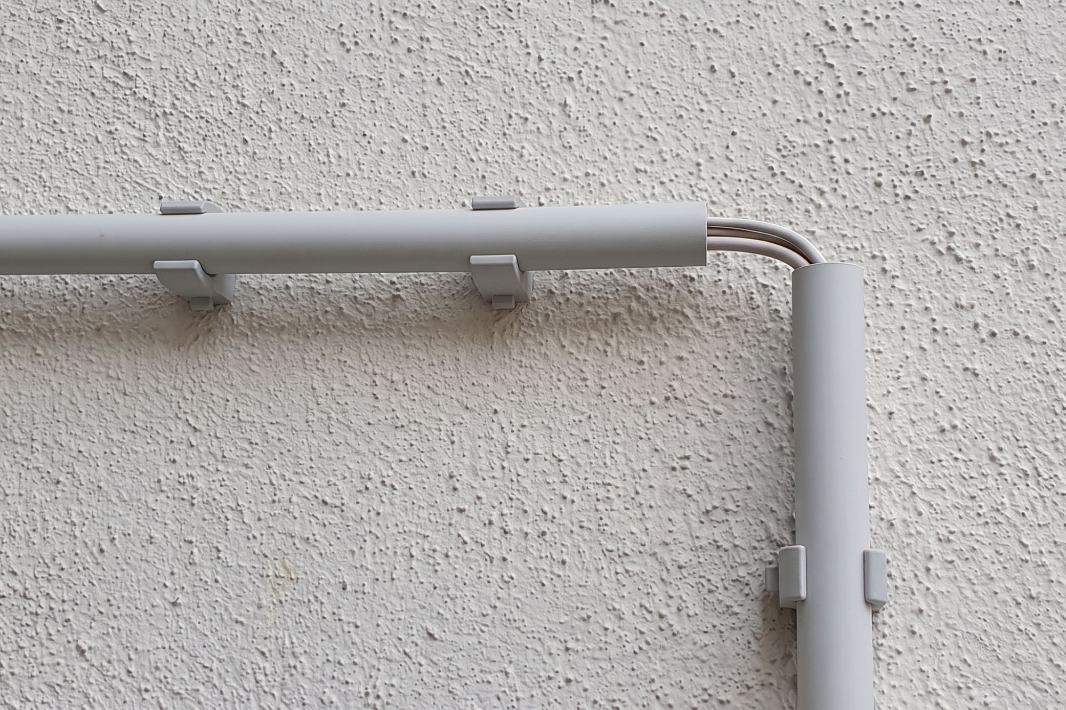 Kabelschellen befestigen hellgraue Kabelrohre und leiten darin enthaltene Drähte ordentlich an einer strukturierten Wand entlang.