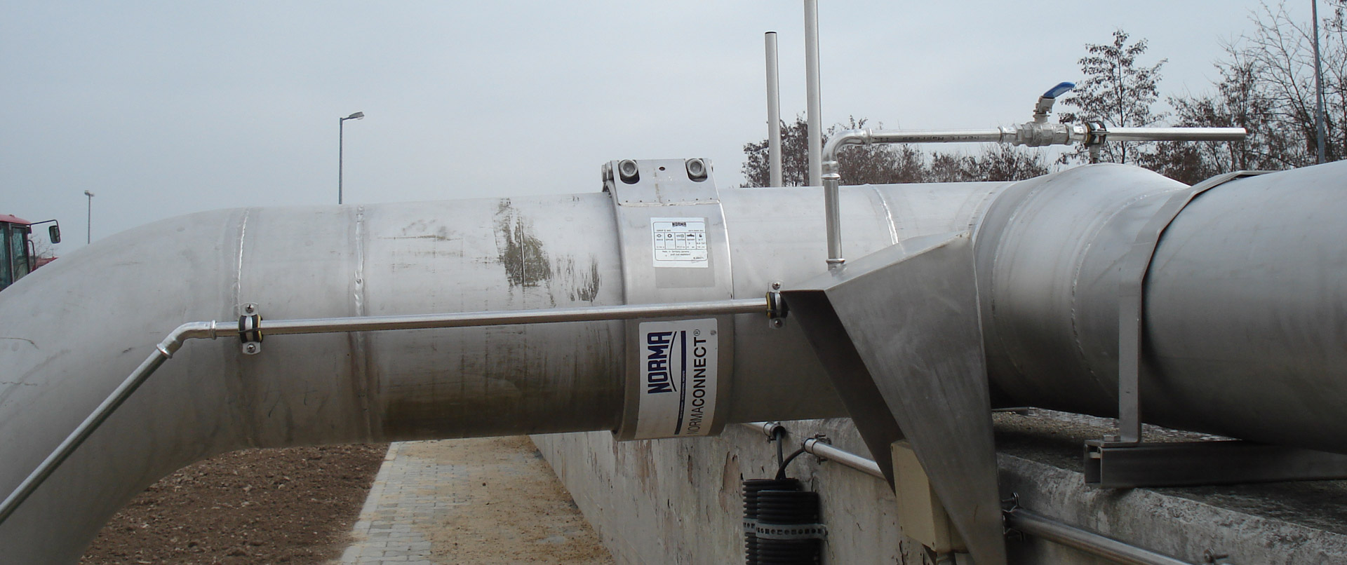 Großes, gebogenes Industrialsystem aus Edelstahlrohren mit einer NORMA NORMACONNECT Rohrkupplung, im Außenbereich installiert.