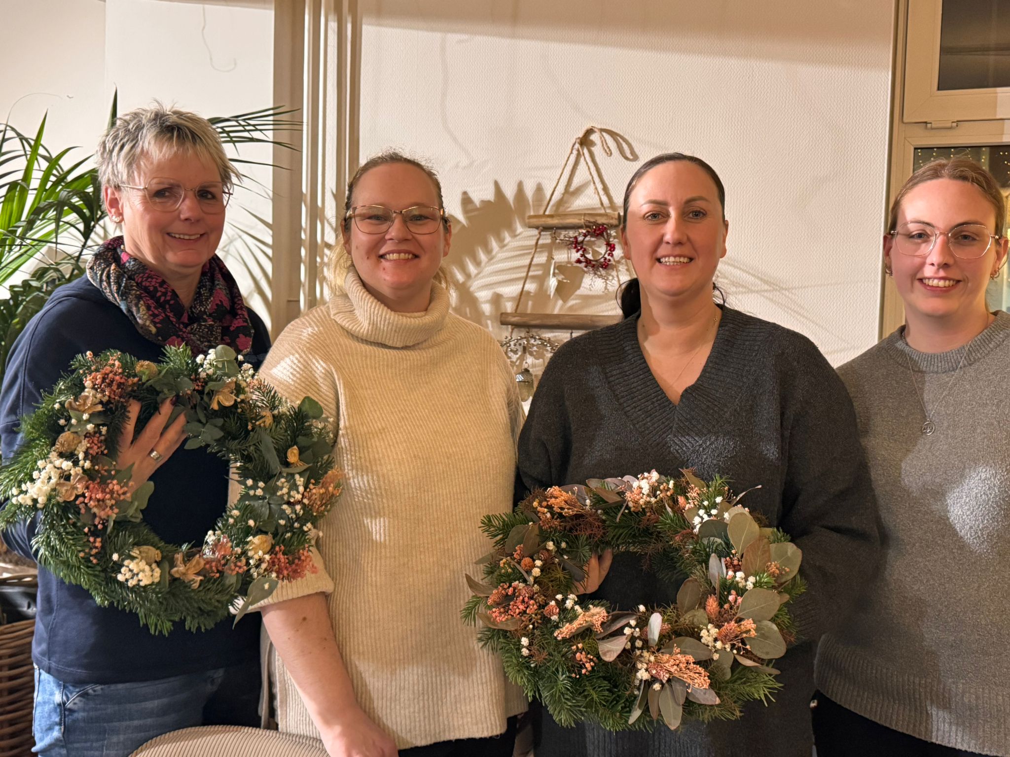 Vier lächelnde Frauen präsentieren stolz ihre selbstgemachten, festlichen Adventskränze aus Tannengrün, Eukalyptus und Trockenblumen, entstanden beim kreativen Teambuilding 'Zauberhafte Vorweihnachtszeit' bei Ly’s.